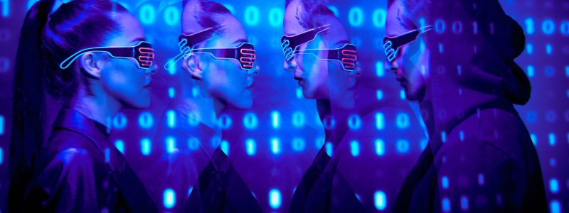 Side view of serious affectionate young couple in neon goggles standing against cyber security background with binary code